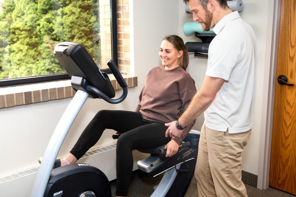 Physical therapist assisting a woman on a recumbent bike during a therapy session.