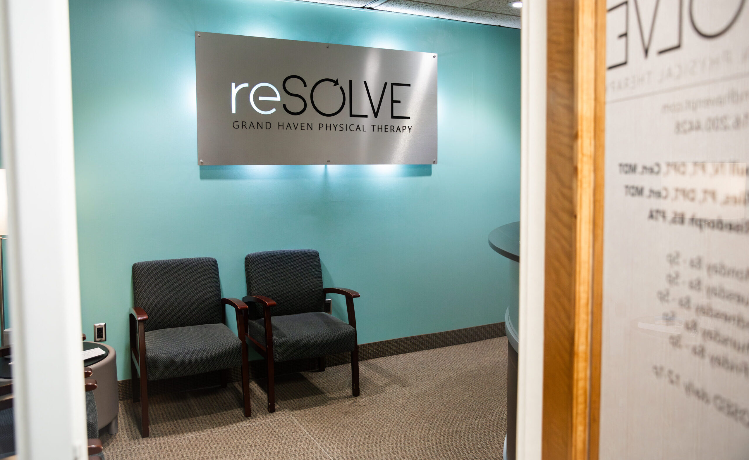 reSOLVE Grand Haven Physical Therapy waiting area with two armchairs and a brushed metal sign on a teal wall.